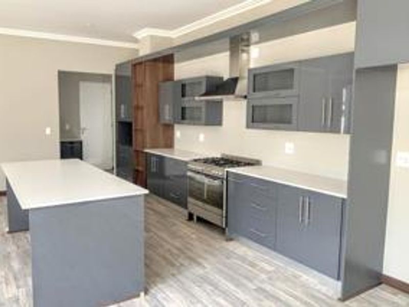Modern kitchen featuring sleek grey cabinetry, a central island with stone countertops, stainless steel gas stove, and durable laminate flooring.