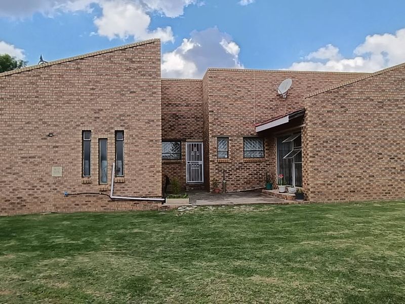 Rear view of a face brick house featuring a built-in brick braai, paved patio area, and a spacious lawn.