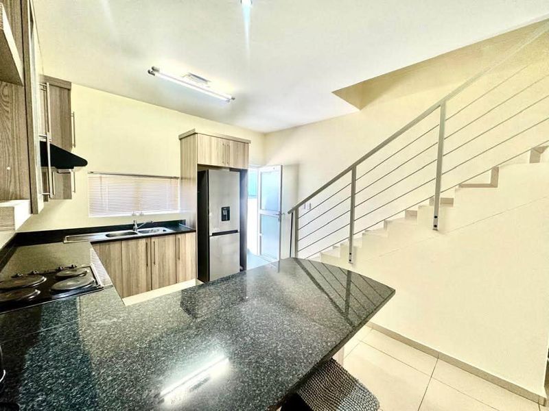 Modern kitchen featuring granite countertops, built-in cabinetry, and an integrated electric hob, adjacent to an open staircase with a contemporary metal railing.