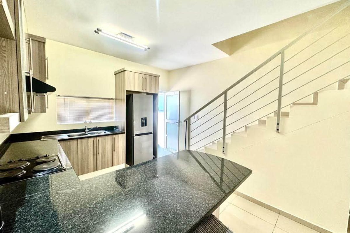 Modern kitchen featuring granite countertops, built-in cabinetry, and an integrated electric hob, adjacent to an open staircase with a contemporary metal railing.