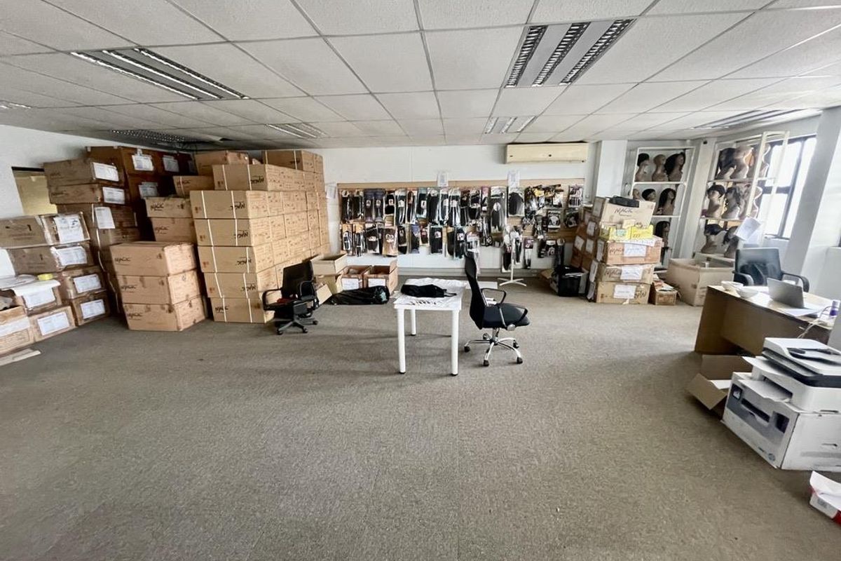 A functional office or commercial space featuring a suspended ceiling, recessed lighting, wall-mounted air conditioning, and carpeted flooring, currently utilized for storage and workspace.