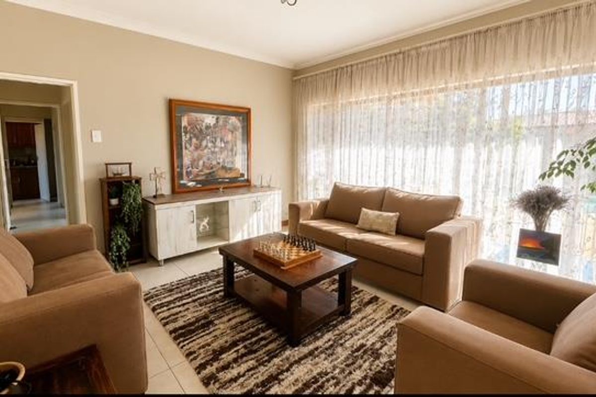 A well-lit living room featuring neutral wall tones, tiled flooring, and a large window with sheer curtains, creating a comfortable and inviting atmosphere.