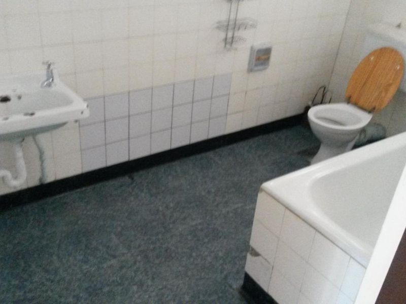 A dated bathroom featuring a wall-mounted basin, standard toilet, and bathtub with tiled walls, requiring modernization to improve its overall condition and appeal.