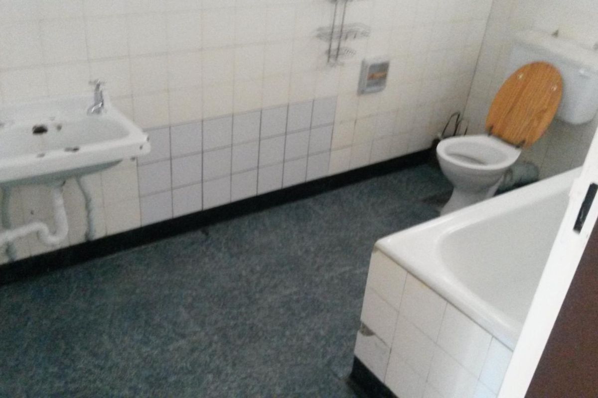 A dated bathroom featuring a wall-mounted basin, standard toilet, and bathtub with tiled walls, requiring modernization to improve its overall condition and appeal.