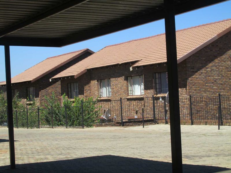 Exterior view of a face brick apartment complex featuring a tiled roof, paved driveway, and covered carport parking area.