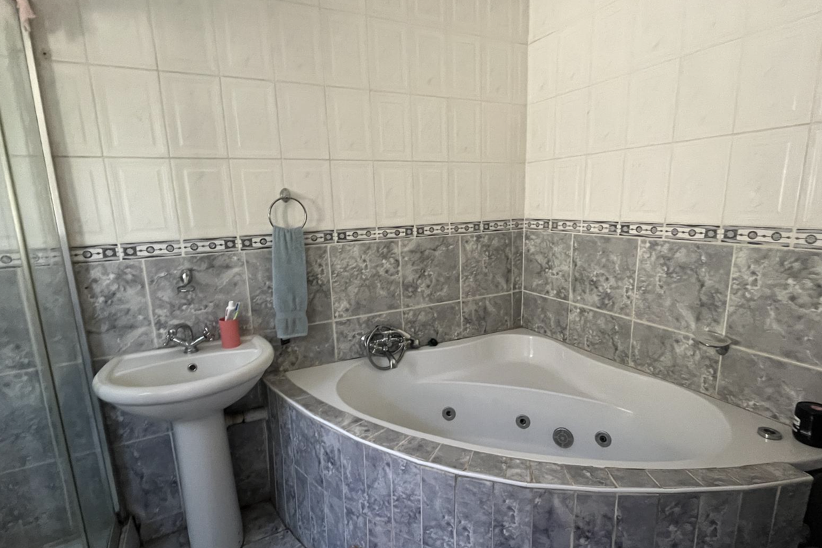 Bathroom featuring a corner spa bath, pedestal basin, and separate shower enclosure with tiled walls and flooring.