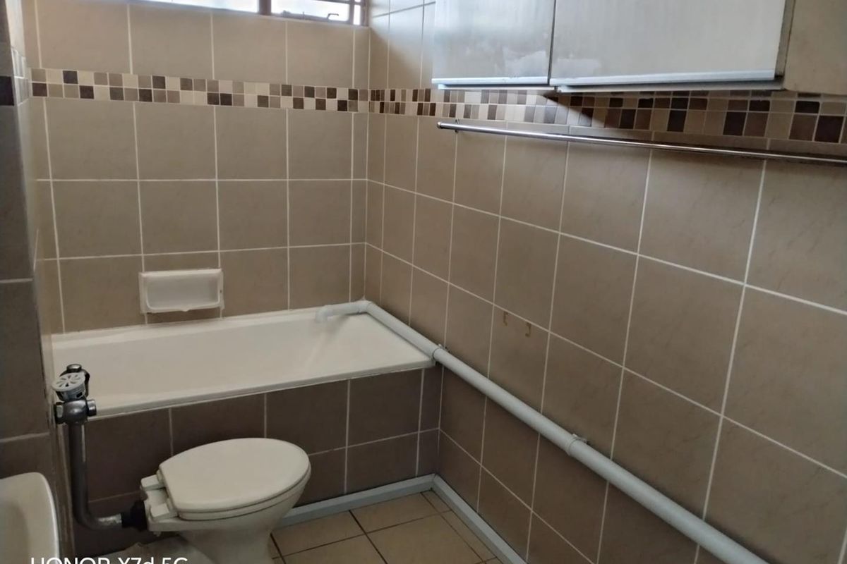 A dated bathroom featuring a standard bathtub, toilet, and wall-mounted cabinetry with exposed surface-mounted plumbing and neutral ceramic tiling.