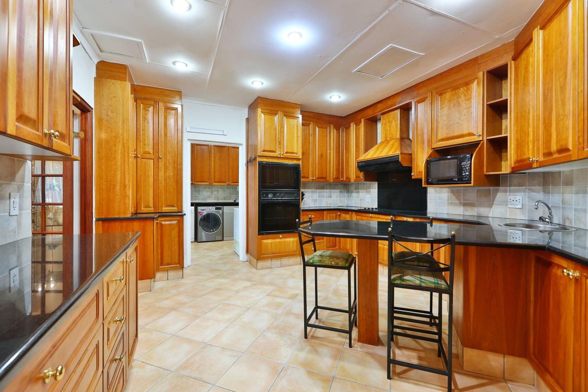 Spacious kitchen featuring extensive timber cabinetry, black granite countertops, built-in double oven, and a breakfast bar, with an adjoining scullery area.