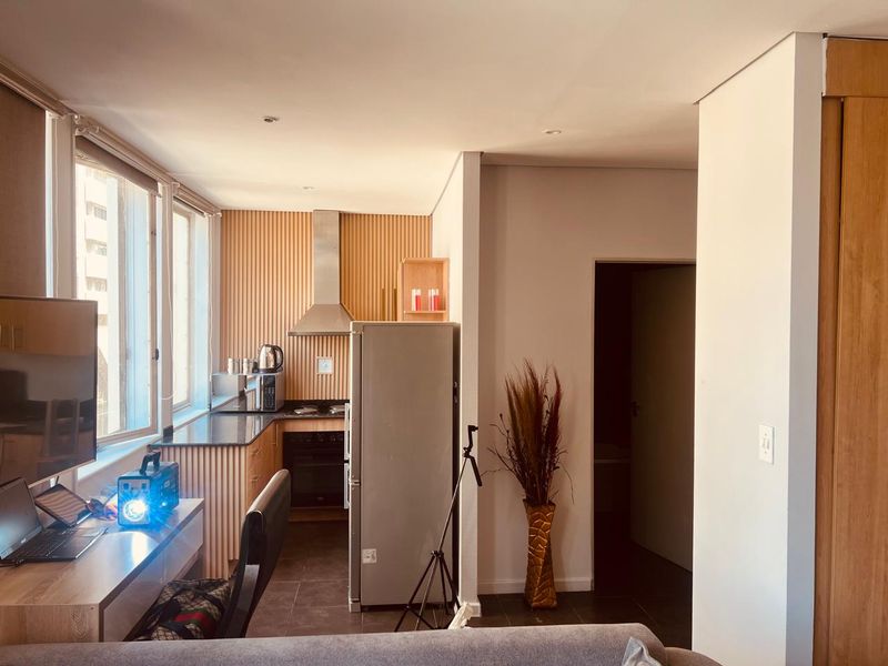 Modern open-plan kitchen area featuring contemporary slatted wood wall paneling, sleek cabinetry, and integrated appliances, seamlessly connected to the living space.