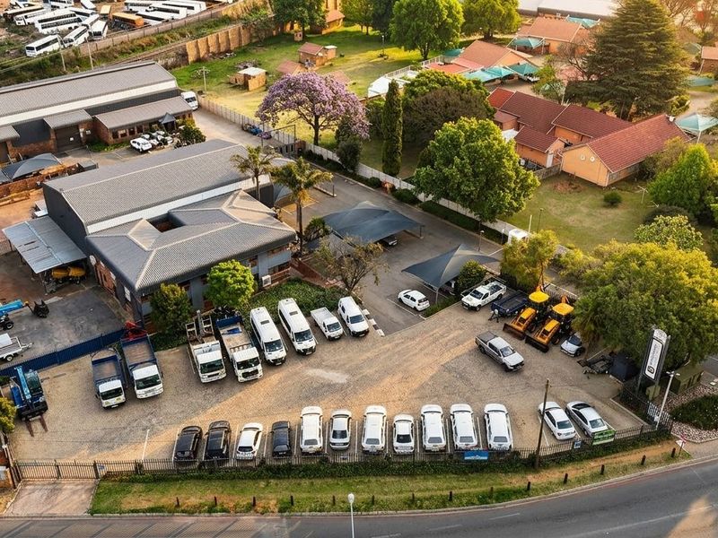 Aerial view of a commercial property featuring industrial warehouse buildings, extensive paved parking with shade cloth structures, and well-maintained landscaped grounds.