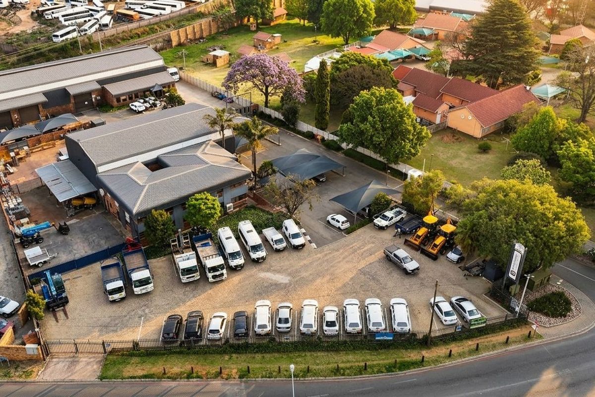 Aerial view of a commercial property featuring industrial warehouse buildings, extensive paved parking with shade cloth structures, and well-maintained landscaped grounds.
