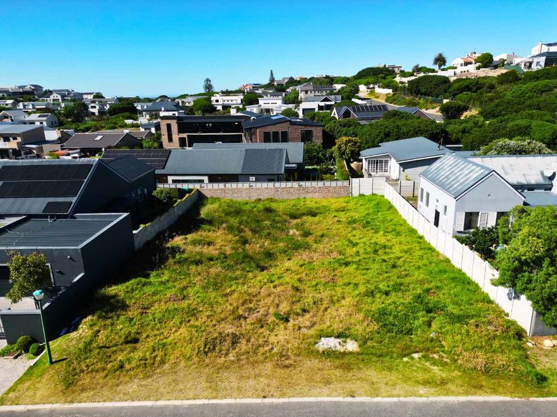 An elevated aerial view of a vacant residential plot situated in a developed neighborhood, featuring boundary walls and direct street access.