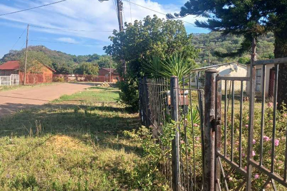 Street view showing the property boundary with a metal fence, gate, and utility infrastructure in a residential neighborhood setting.