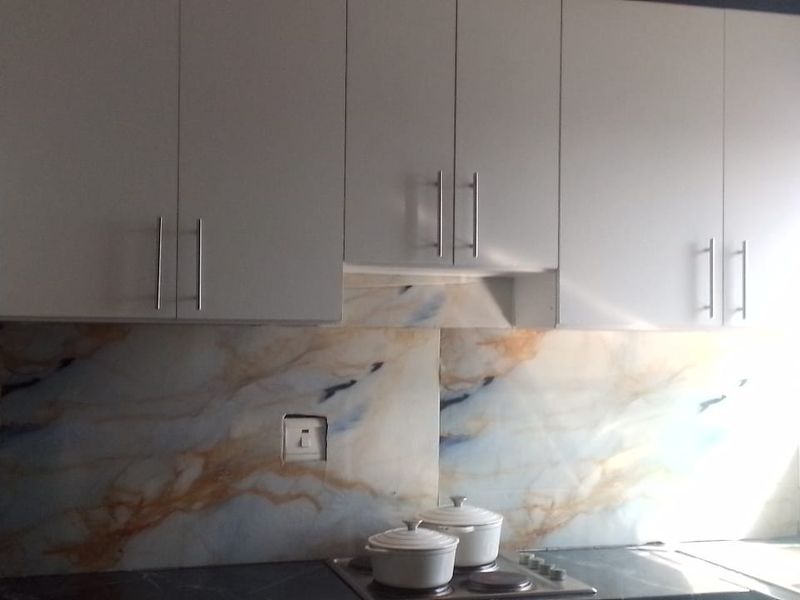 A functional kitchen featuring white cabinetry, a marble-effect splashback, an electric hob, and a stainless steel sink with natural light.