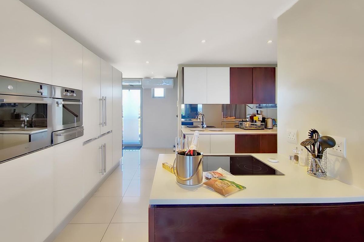Modern kitchen featuring sleek white and dark wood cabinetry, integrated stainless steel ovens, a central island with a built-in induction hob, and tiled flooring.