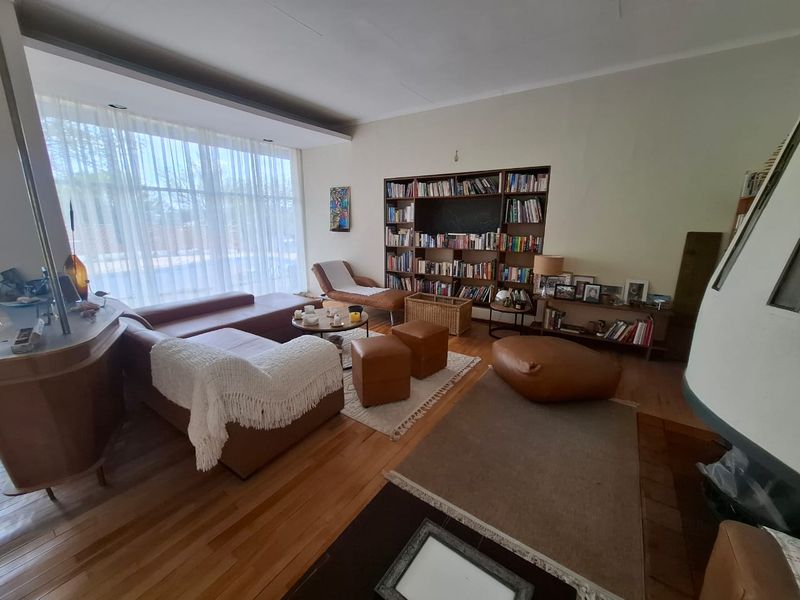 Spacious living room featuring warm hardwood flooring, a large floor-to-ceiling window, and a custom built-in bookshelf, creating a comfortable and inviting atmosphere.