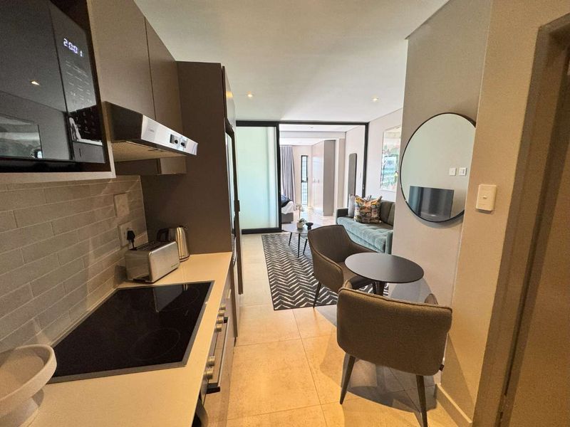 Modern open-plan apartment featuring a sleek kitchen with integrated appliances, tiled flooring, and seamless flow into the living area through a sliding glass door.