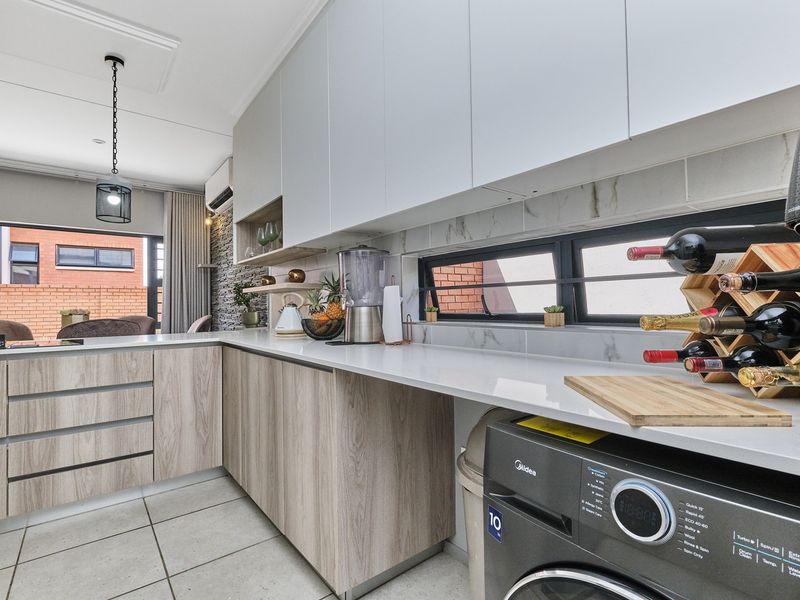 Modern kitchen featuring sleek wood-grain and white cabinetry, stone countertops, tiled flooring, and a stylish stone feature wall.