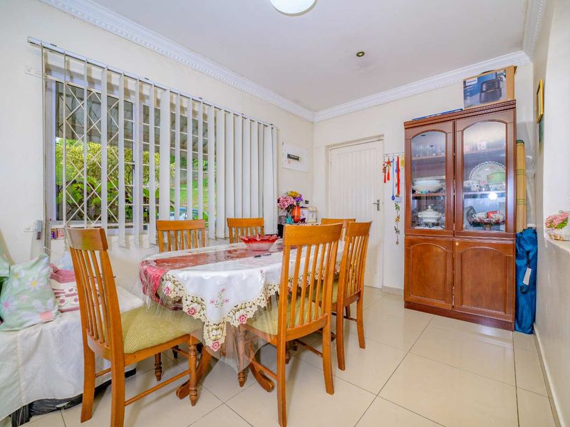 A dining room featuring tiled flooring, decorative ceiling cornicing, and a large window fitted with security bars and vertical blinds.