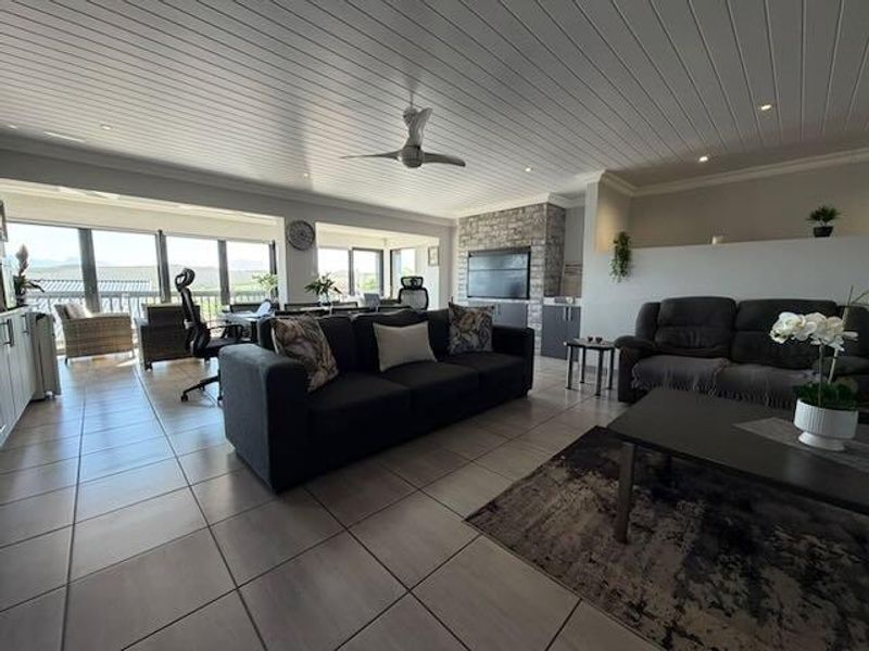 Spacious open-plan living area featuring tiled floors, a tongue and groove ceiling with a fan, and a stone feature wall with large sliding doors.