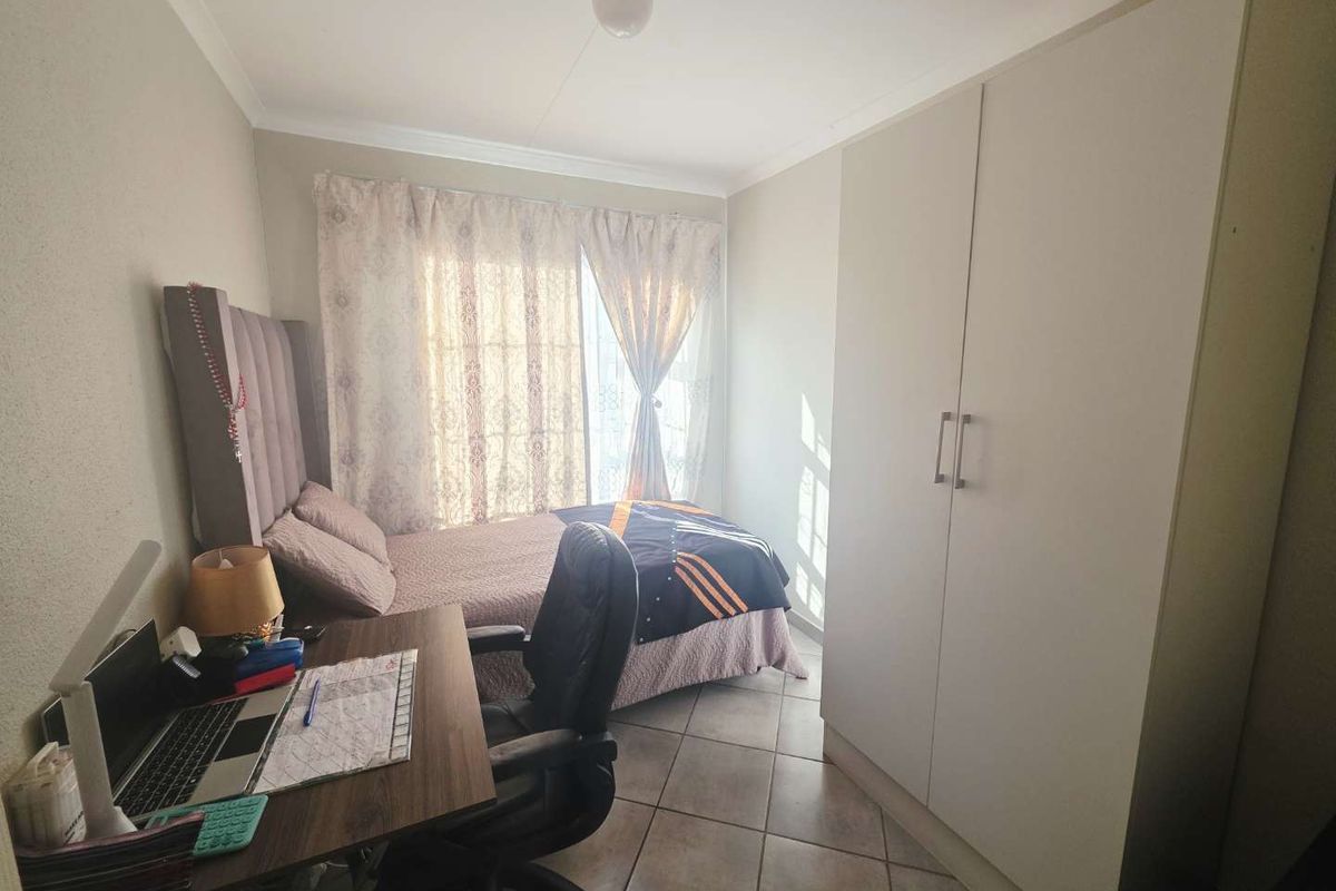 A functional bedroom featuring tiled flooring, a built-in wardrobe, and natural light through the window.