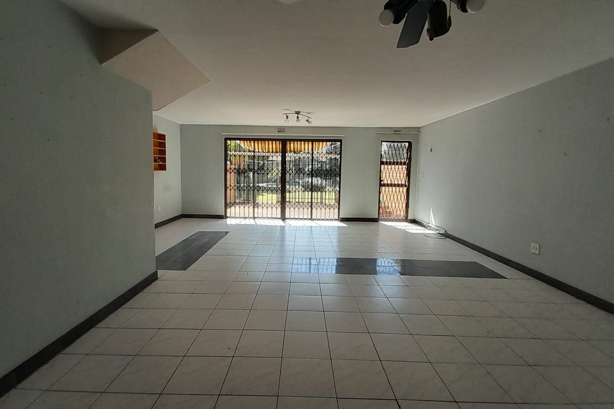 A spacious, empty living area featuring neutral tiled flooring, ceiling fan, and secure sliding glass doors leading to the outdoor space.