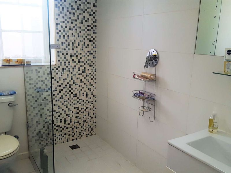 A functional bathroom featuring a shower enclosure with mosaic tile accents, a white vanity basin, and a wall-mounted mirror.