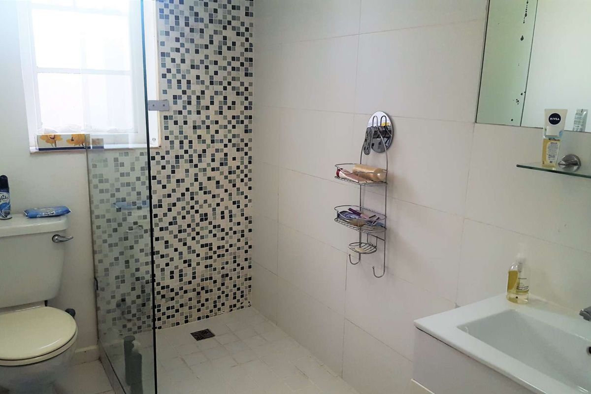 A functional bathroom featuring a shower enclosure with mosaic tile accents, a white vanity basin, and a wall-mounted mirror.