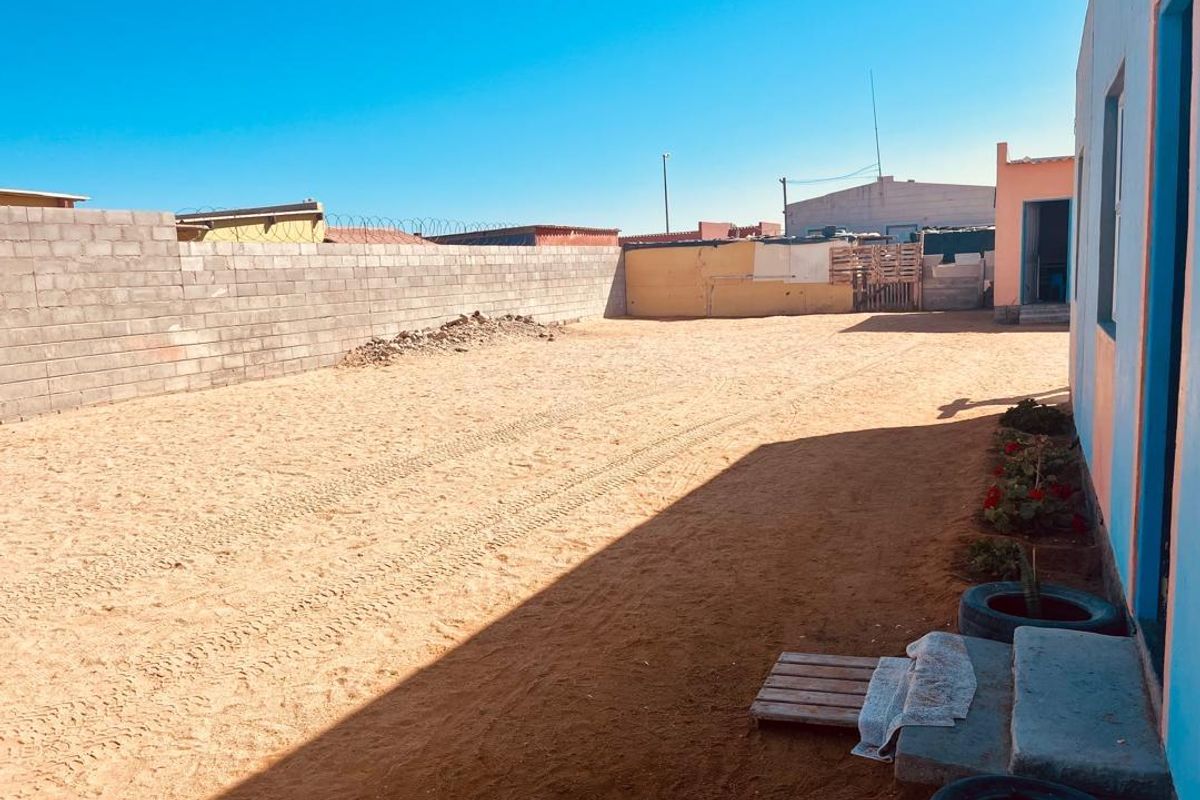 A large, undeveloped rear yard featuring a concrete block boundary wall with security wire, offering significant potential for landscaping or outdoor improvement.