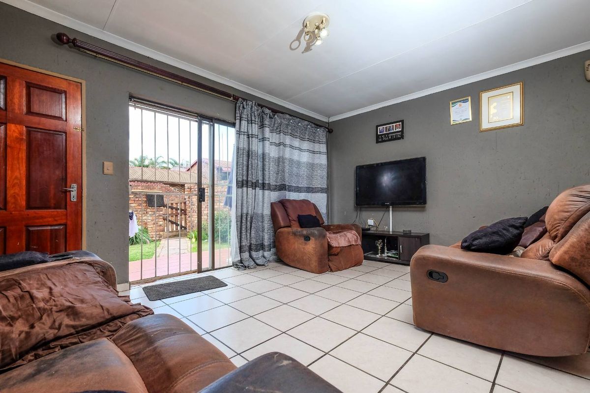 A living room featuring tiled flooring, a sliding glass door with security gate, and direct access to the rear garden area.