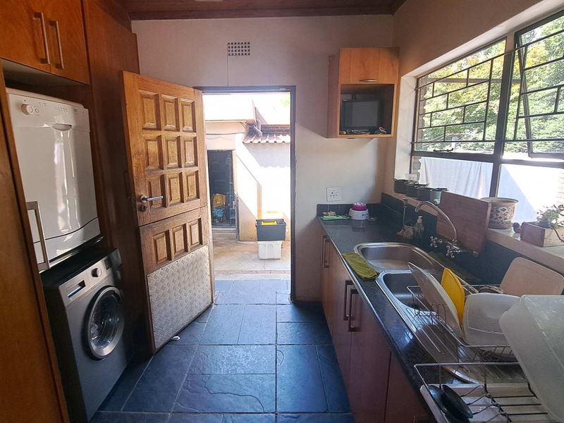 Functional scullery featuring built-in cabinetry, granite countertops, double basin sink, and direct access to the rear exterior area.