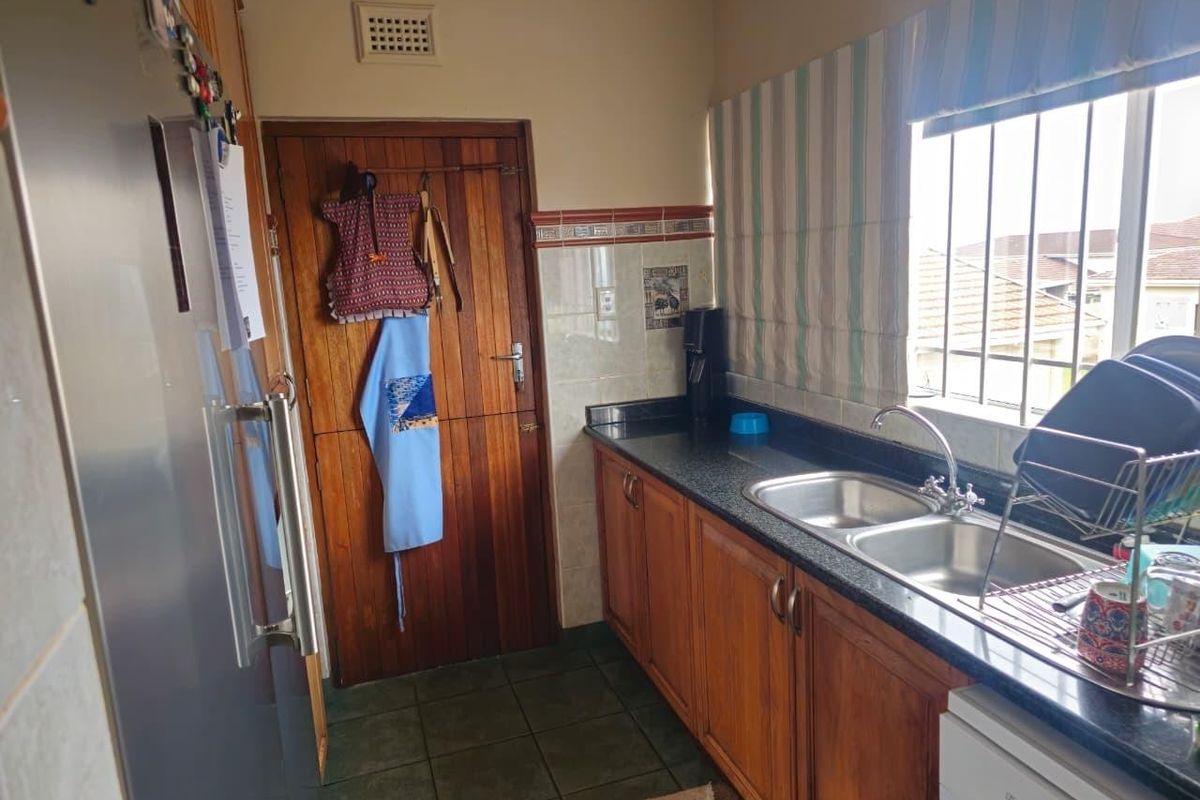 A functional kitchen featuring wooden cabinetry, granite countertops, a double bowl stainless steel sink, and tiled flooring with a window providing natural light.