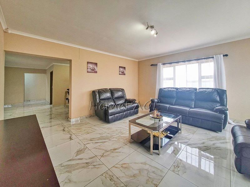 Spacious living room featuring polished marble-look porcelain floor tiles, neutral wall tones, and large windows allowing for ample natural light.