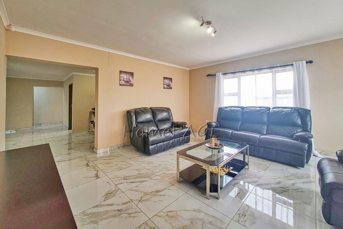 Spacious living room featuring polished marble-look porcelain floor tiles, neutral wall tones, and large windows allowing for ample natural light.