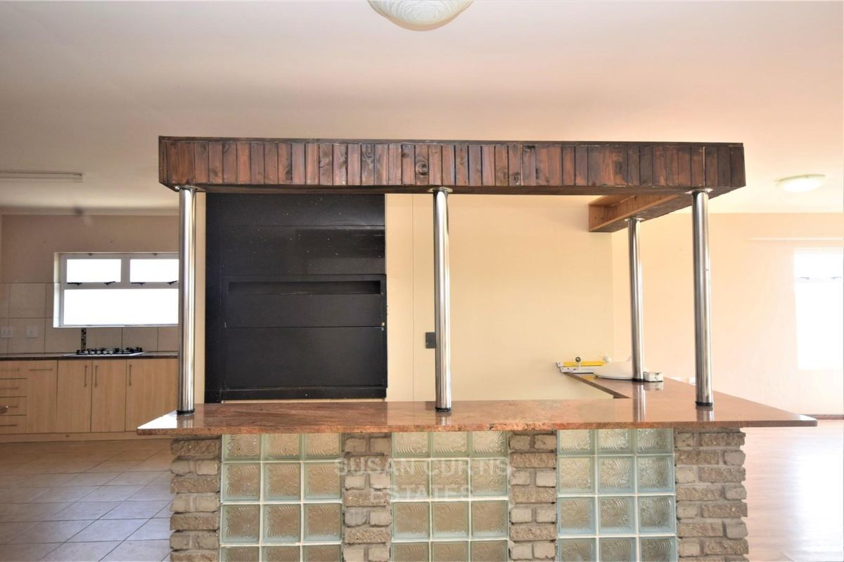 A spacious kitchen featuring a unique glass block breakfast bar with granite countertop, timber bulkhead, and integrated cooking appliances.