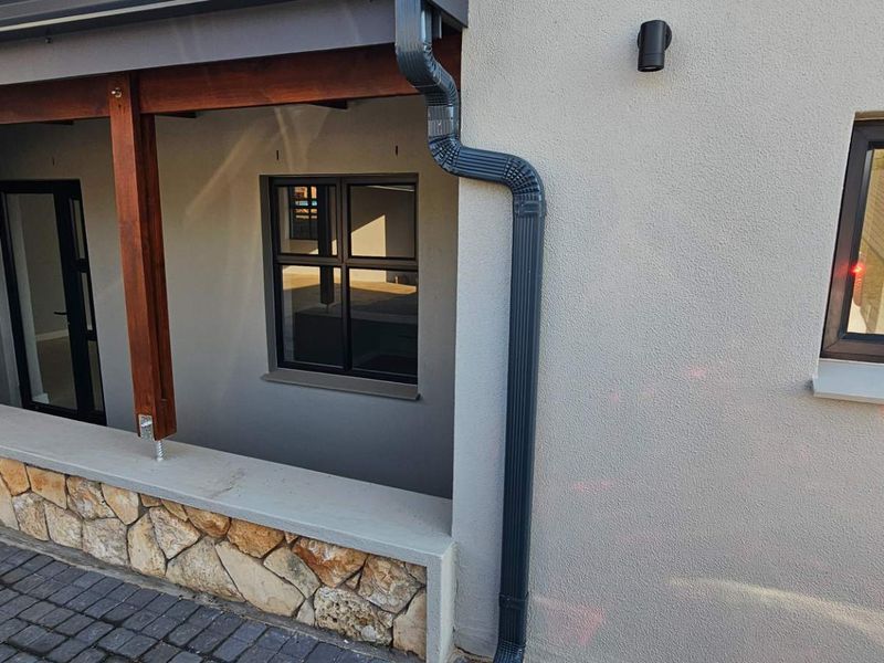 A modern covered patio area featuring stone cladding, timber support beams, and contemporary aluminium window frames.