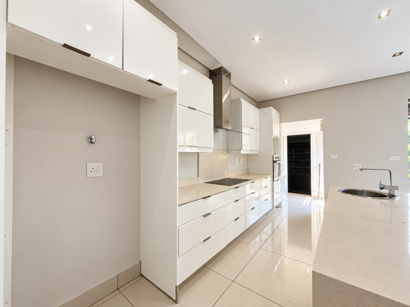 Modern kitchen featuring sleek white cabinetry, stone countertops, integrated appliances, and high-gloss floor tiles, offering a clean and contemporary culinary space.