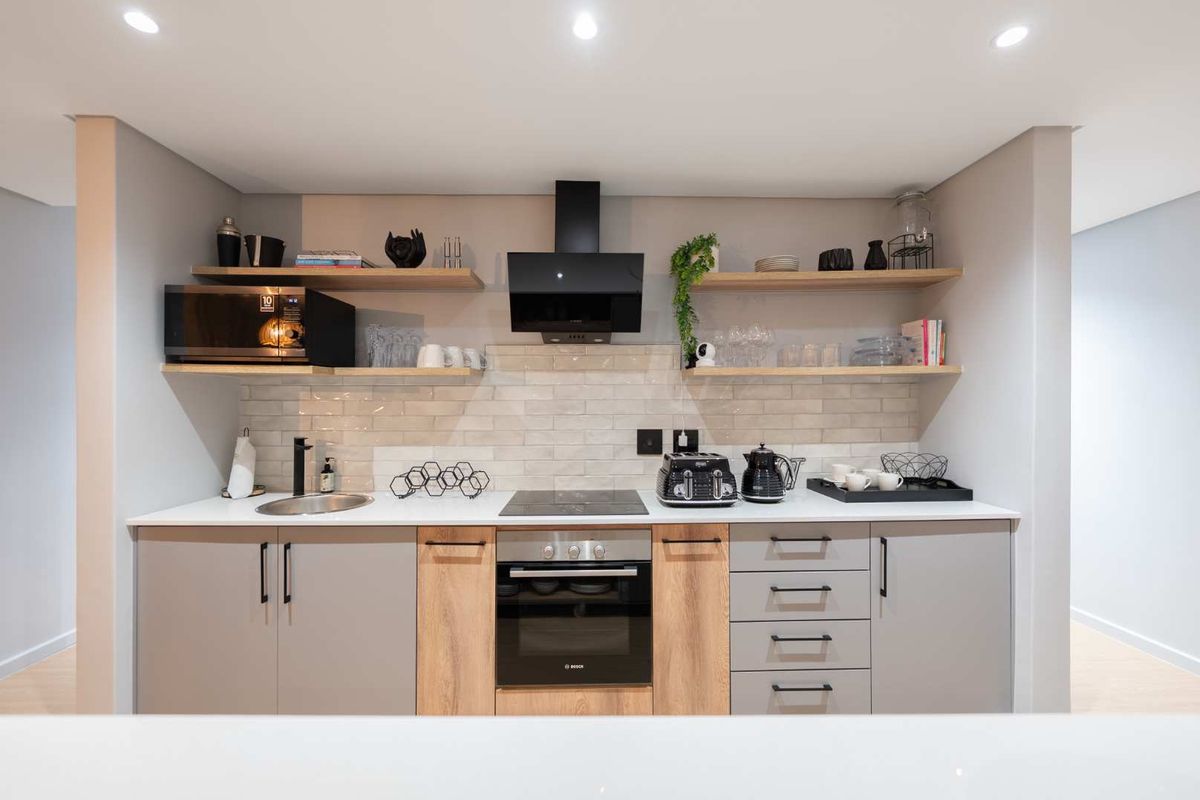 A modern, well-appointed kitchen featuring sleek cabinetry, timber shelving, a subway tile backsplash, and integrated appliances including an oven and hob.