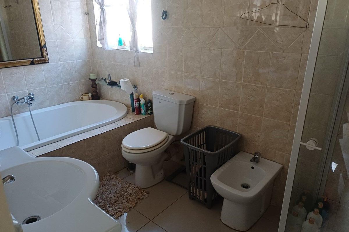 A functional bathroom featuring a built-in bathtub, toilet, bidet, vanity basin, and a separate shower enclosure with neutral ceramic tiling throughout.