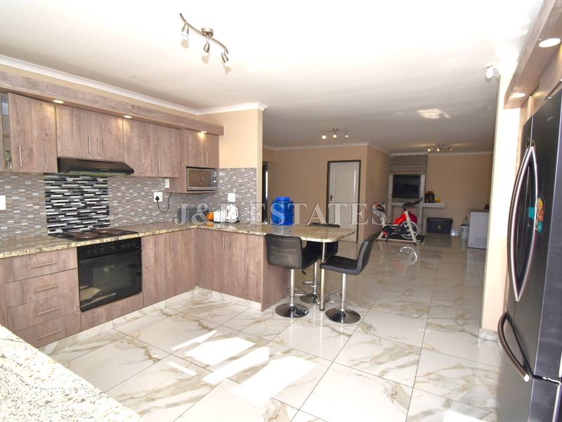 Spacious open-plan kitchen featuring granite countertops, built-in appliances, and modern tiled flooring, flowing into a versatile living area.