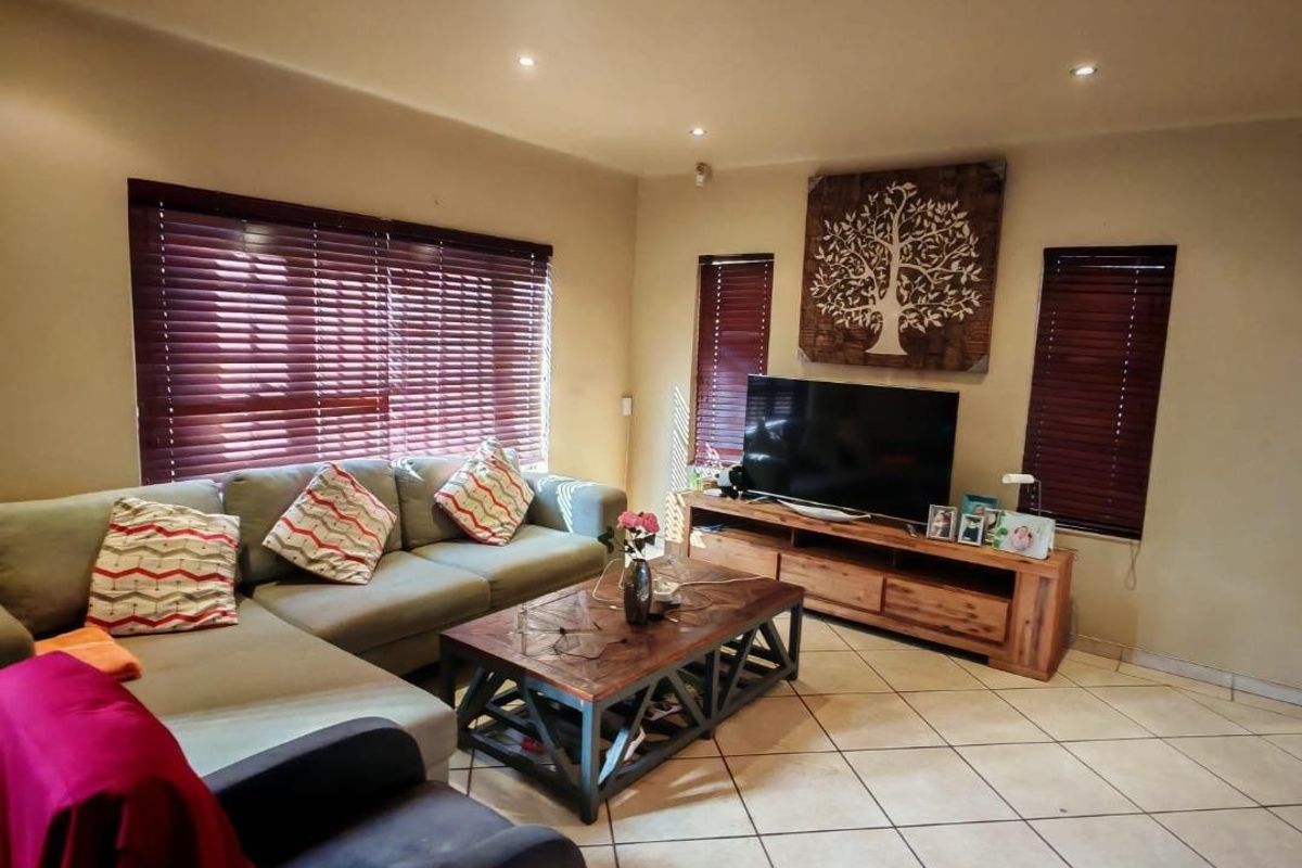 A comfortable living room featuring ceramic floor tiles, recessed downlighting, and multiple windows fitted with dark wood-tone venetian blinds.