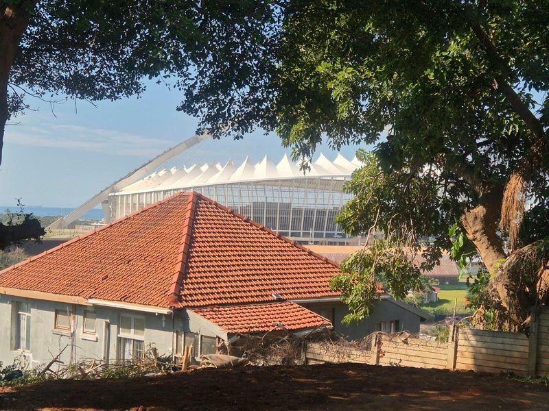 An elevated view overlooking a residential property with terracotta roof tiles, featuring a prominent view of a large stadium in the background.