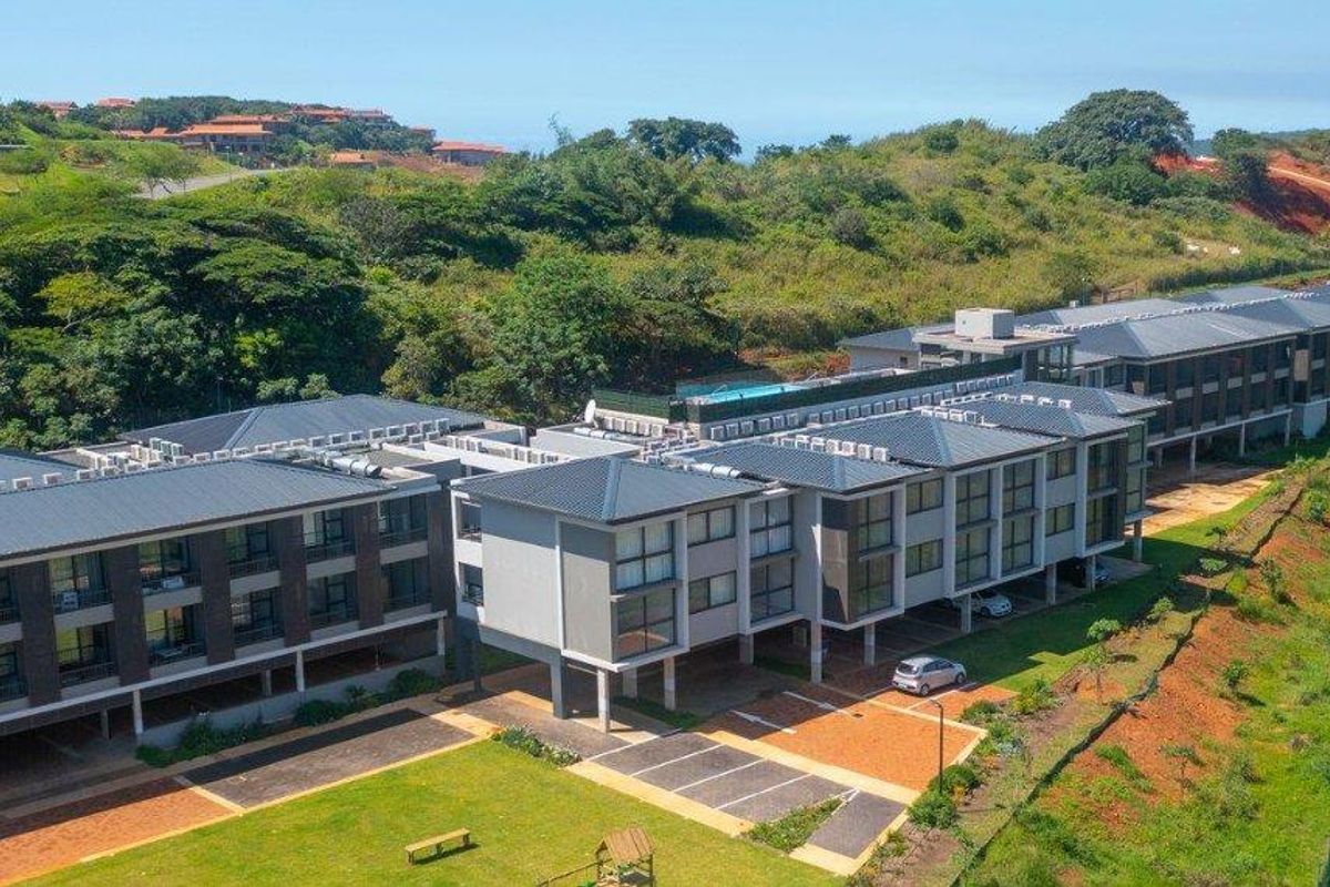 Aerial view of a modern apartment complex featuring multiple levels, balconies, a swimming pool, and paved parking areas set within a landscaped estate.