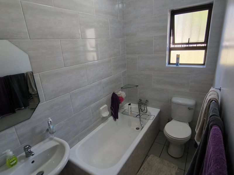 A functional bathroom featuring a bathtub, pedestal basin, and toilet with neutral wall tiling and natural light from a window.