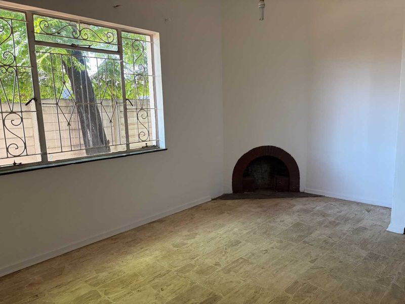 An empty living room featuring a traditional brick fireplace, tiled flooring, and large windows fitted with metal security bars.