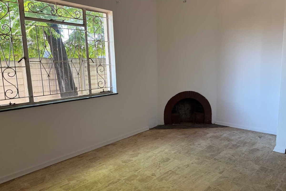 An empty living room featuring a traditional brick fireplace, tiled flooring, and large windows fitted with metal security bars.
