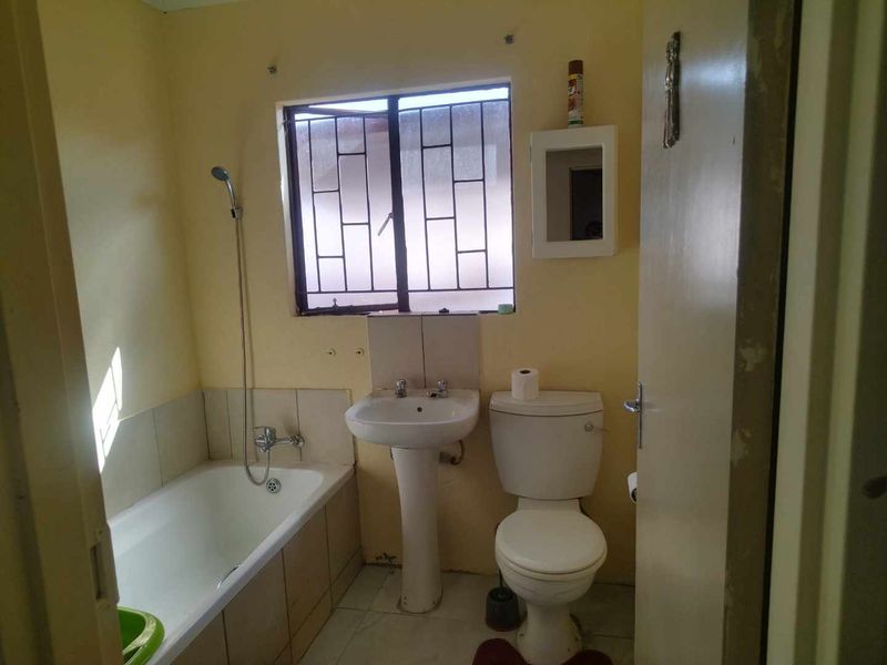 A functional bathroom featuring a pedestal basin, toilet, and bathtub with a shower mixer, requiring cosmetic updates to improve its overall condition.