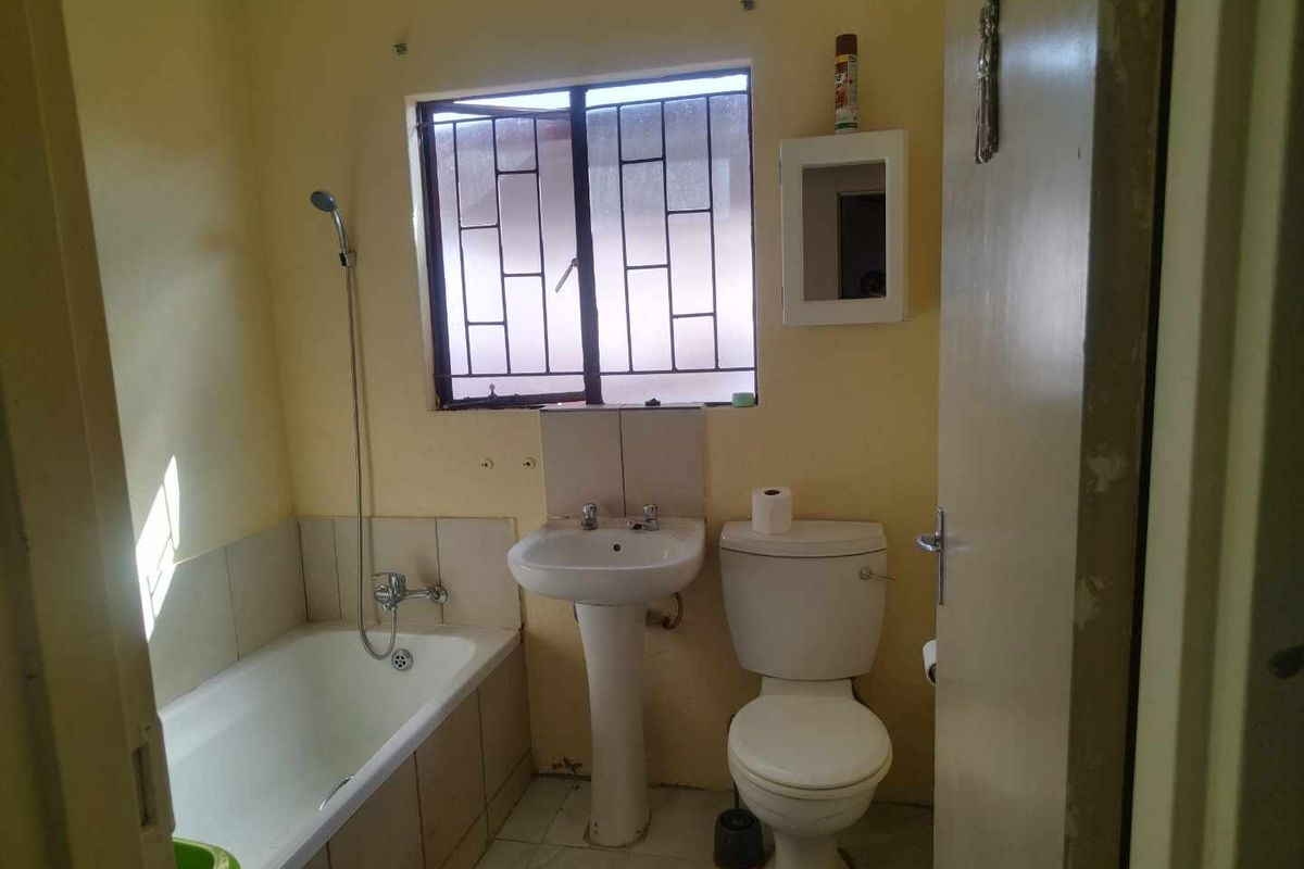 A functional bathroom featuring a pedestal basin, toilet, and bathtub with a shower mixer, requiring cosmetic updates to improve its overall condition.