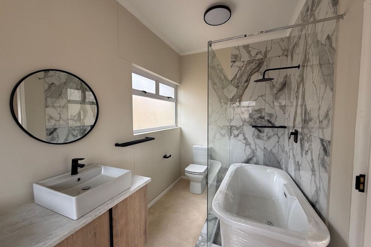 Modern bathroom featuring a marble-look tiled shower enclosure, freestanding bathtub, vessel sink vanity, and contemporary black fixtures.