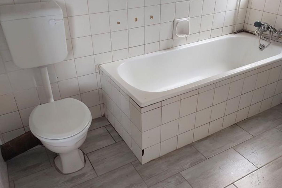 A dated bathroom featuring a standard bathtub, wall-mounted toilet, and tiled flooring. The space requires cosmetic updates to improve its overall condition.
